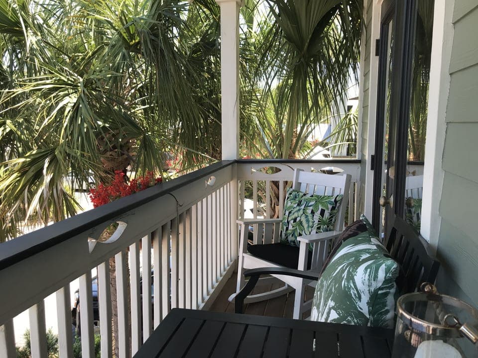 Front deck with bar height table and chairs nestled in palm trees
