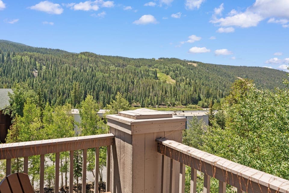 A sunlit balcony frames sweeping mountain vistas of forested slopes and the valley below, offering an ideal spot to savor your morning coffee or unwind after a day of adventure.